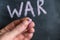 A grown man holds a piece of colored chalk in his hand. Handwritten word WAR on black chalkboard