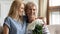 Grownup daughter congratulate mature mom with flowers