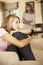 Grumpy Teenage Daughter Sitting On Sofa With Mother In Background