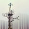 Grunge communication equipment construction on building background. Metal tower with antennas against the foggy sky