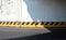 Grunge concrete wall of an underpass  with a yellow and black guard rail divided in two by the shadow of the bridge