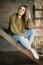 Grunge fashion: cute young girl informal model in blue jeans, dark knitted sweater and white socks sitting on the ladder