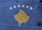 Grunge Kosovo flag texture, a blue field charged with a map of Kosovo in gold, surmounted by an arc of six white star.