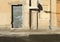 Grunge peeled plaster facade with an old store shutter closed, a gutter and a road sign. Sidewalk and paved street in front.