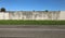 Grunge white plaster surrounding wall with strip of grass and road in front.