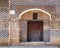 Grunge wooden decorated arched gate with inner small door on wall with black and red bricks