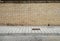 Grunge yellow brick wall with a sidewalk made of concrete tiles and an asphalt street.