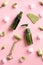 Gua Sha massage tool, jade stone face roller and green cosmetic bottles on pink background with ice cubes and flowers. Facial skin