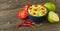 Guacamole in blue bowl on natural rustic desk with ingredient: lemon, tomatoes, peppers around.