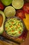 Guacamole in blue bowl on natural rustic desk with ingredient: lemon, tomatoes, peppers around.