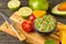 Guacamole in blue bowl on natural rustic desk with ingredient: lemon, tomatoes, peppers around.