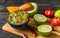 Guacamole in blue bowl with tortilla chips and lemon on natural wooden desk.