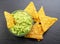 Guacamole sauce and tortilla chips, popular Mexican food, on slate serving board. Top view