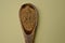 Guarana powder in a wooden spoon on a yellow pastel background.