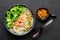 Guay Tiew Gai Cheek or Thai Chicken Noodle Soup in black bowl on dark slate backdrop. Thai food