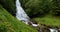 Gudvangen-Naeroyfjorden, Norway. Waterfall Tuftofossen In Spring. Young Caucasian Woman Lady Tourist Traveler