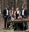 Guests and a couple of newlyweds near the picnic table in the woods