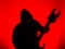 Guitarist with hood and a pointed Heavy Metal guitar with horned headstock on red background