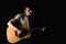 Guitarist, music. A young man plays an acoustic guitar on a black isolated background. Horizontal frame