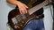 Guitarist plays on a brown bass in studio, dressed in jeans and a black shirt