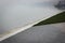 The Gull Stands On The Concrete Pond Embankment, And Behind It, You Can See The Pond Covered With Mist