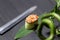 Gunkan Sake Green sushi with salmon and black tobiko caviar served in cucumber on bamboo leaf near Japanese knife.
