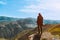 A guy with a camera stands on a cliff and looks fascinated at the mountains