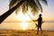 The guy enjoys the sunset riding on a swing on the ptropical beach. Silhouettes of a guy on a swing hanging on a palm tree,