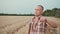 guy farmer stands in the field, wipes sweat after harvesting, looks into the distance and into the camera.