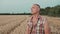 guy farmer stands in the field, wipes sweat after harvesting, looks into the distance and into the camera.