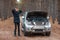 A guy is frustrated holding head while standing near a broken car with an open hood in the smoke. In the autumn forest.