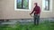 Guy gardener mows tall green grass with gasoline lawn mower, afternoon, near house