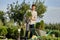 Guy gardener puts the seedlings in pots in a cart on the garden path in the wonderful nursery-garden on a sunny day