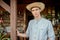 Guy gardener in a straw hat is standing next to a wooden veranda on a sunny day.