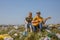 A guy and a girl with a guitar sit on a green hillock littered with plastic trash