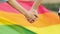 A guy with a girl holding hands against the background of a rainbow flag, close-up. Hands of a young couple against the