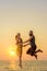 Guy and girl jumping in the air on the background of the sea and looking at camera. Young happy couple jumps on the beach at