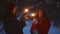 A guy and a girl light sparklers in the winter forest for Christmas.