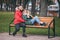 A guy and a girl are resting on a bench in an autumn park. A loving couple in jackets sits on a bench in the main park