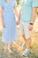 Guy and girl are standing holding hands on dry grass. Cropped. Faceless