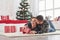 Guy gives his wife christmas gift. Lovely young couple lying on the living room with green holiday tree at background