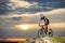 Guy in glasses, helmet and sportswear riding on the mountain bicycle on cliff against evening sky