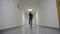 Guy goes strange gait in the long white corridor