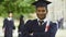 Guy in graduation outfit crossing arms with diploma in hand, smiling achievement