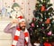 Guy in hat and scarf sits by Christmas tree