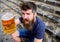 Guy having rest with cold draught beer. Hipster on cheerful face drinking beer outdoor, raising drink up. Man with beard