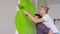 The guy holds the girl on his back, the girl paints the wall with a roller in green