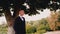 A guy in a jacket stands under a big tree and looks away