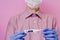 A guy in a mask and a medical glove holds a thermometer. Pink background.