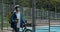 Guy in medical mask with transportation bag pushing bike near sports field. Bicycle courier in protective cycling helmet